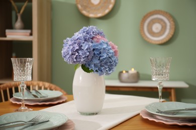 Photo of Stylish setting with plates and vase of flowers on wooden table in dining room, closeup. Interior design