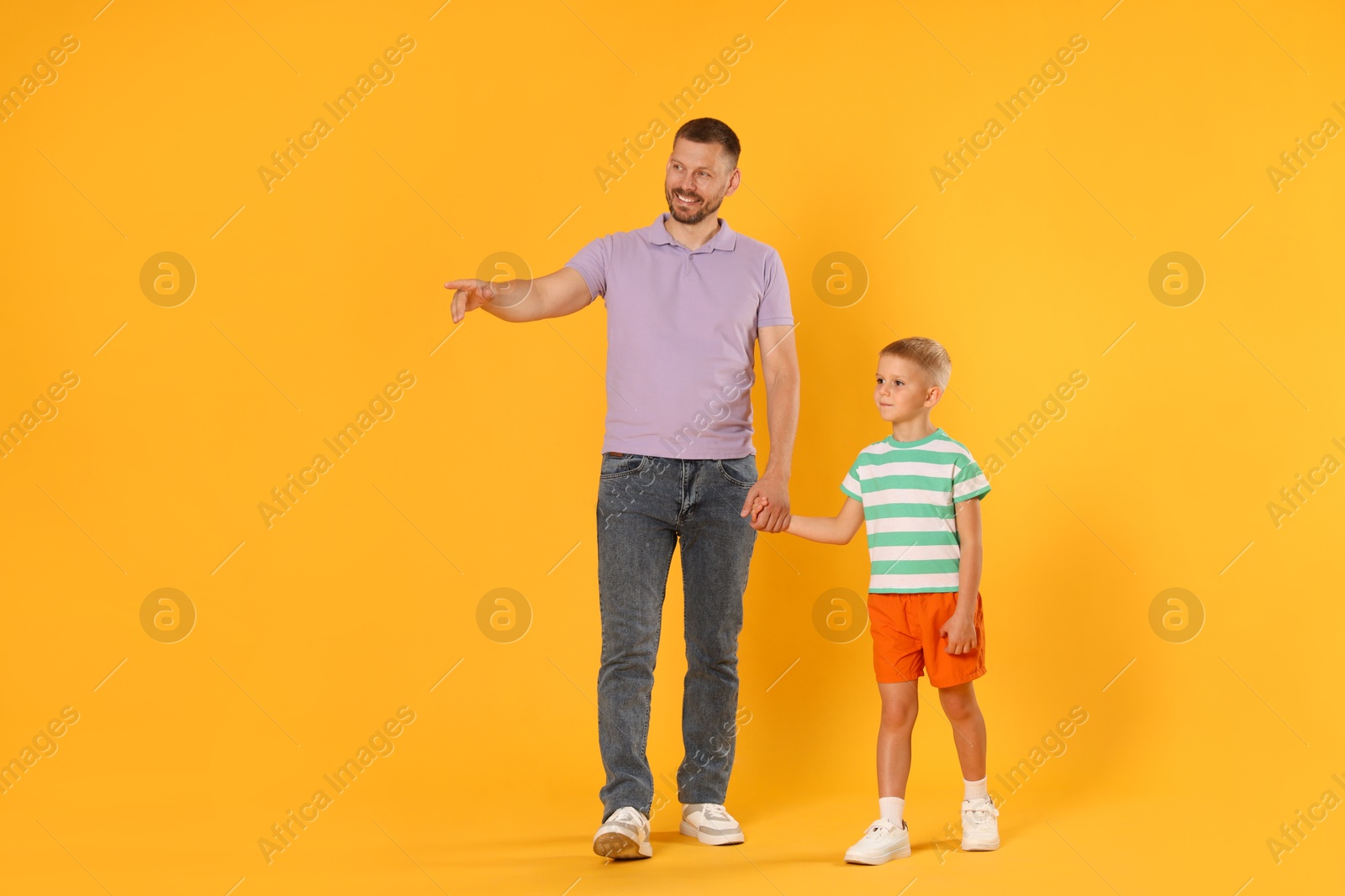 Photo of Happy father showing his son something on yellow background