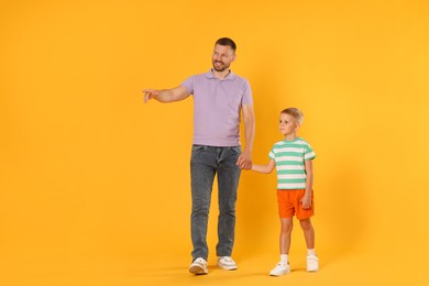 Photo of Happy father showing his son something on yellow background