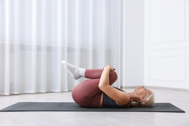 Photo of Mature woman in sportswear stretching on mat near window at home