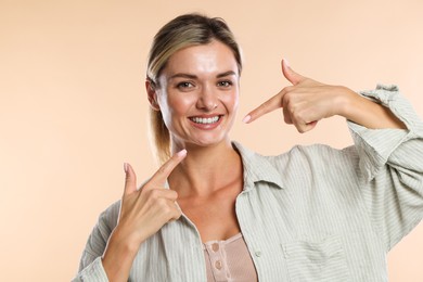 Photo of Woman pointing at her healthy teeth on beige background