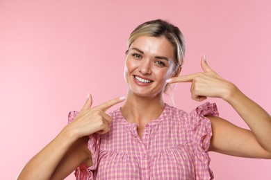 Photo of Woman pointing at her healthy teeth on pink background