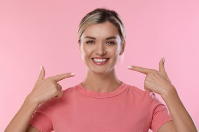 Photo of Woman pointing at her healthy teeth on pink background