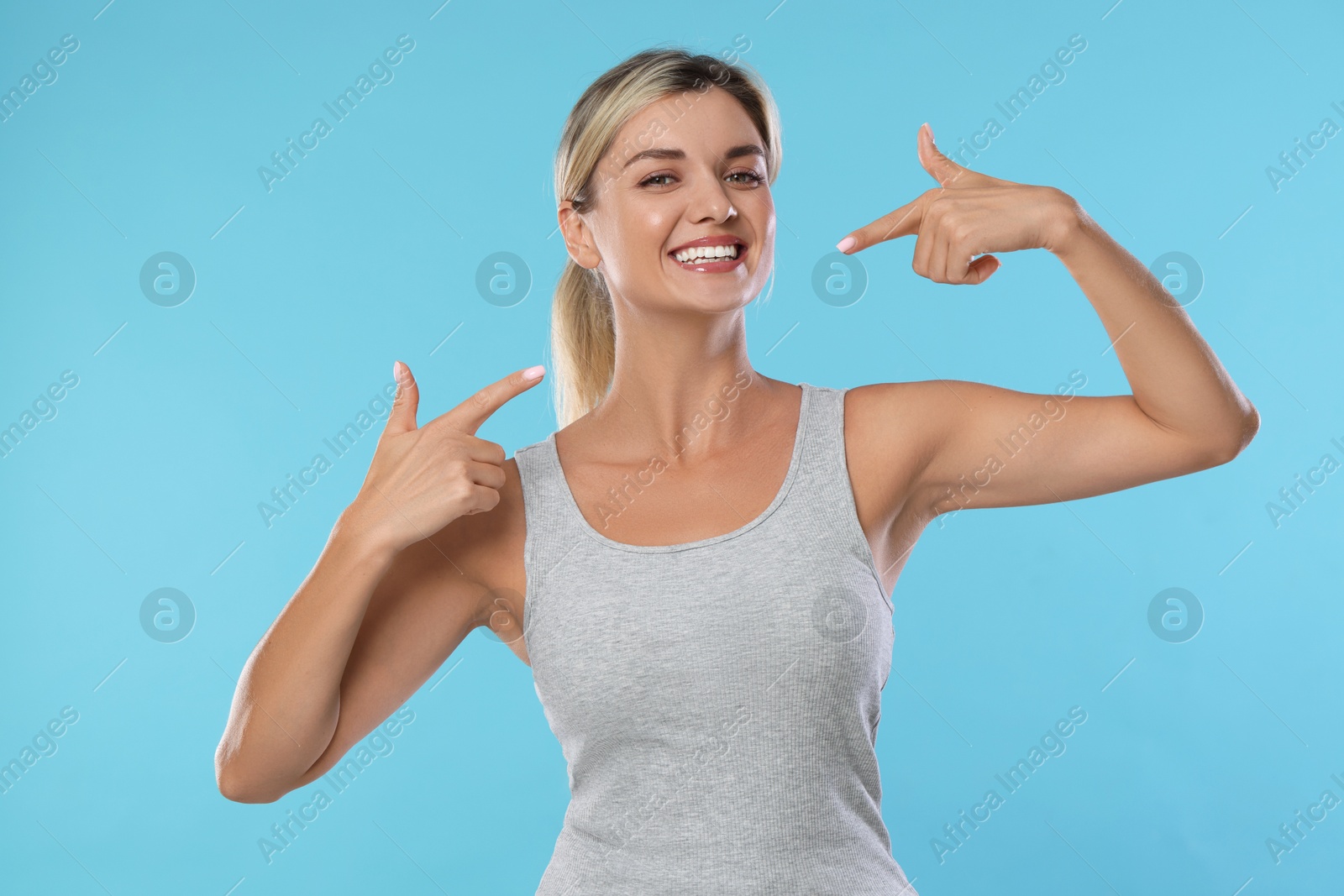 Photo of Woman pointing at her healthy teeth on light blue background