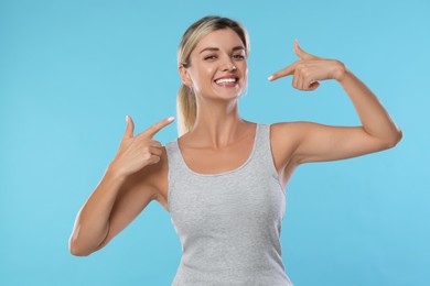 Photo of Woman pointing at her healthy teeth on light blue background