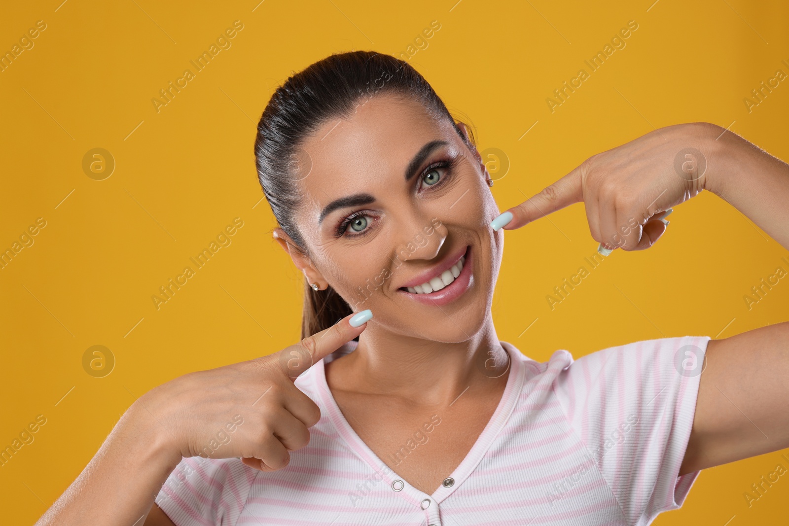 Photo of Woman pointing at her healthy teeth on yellow background
