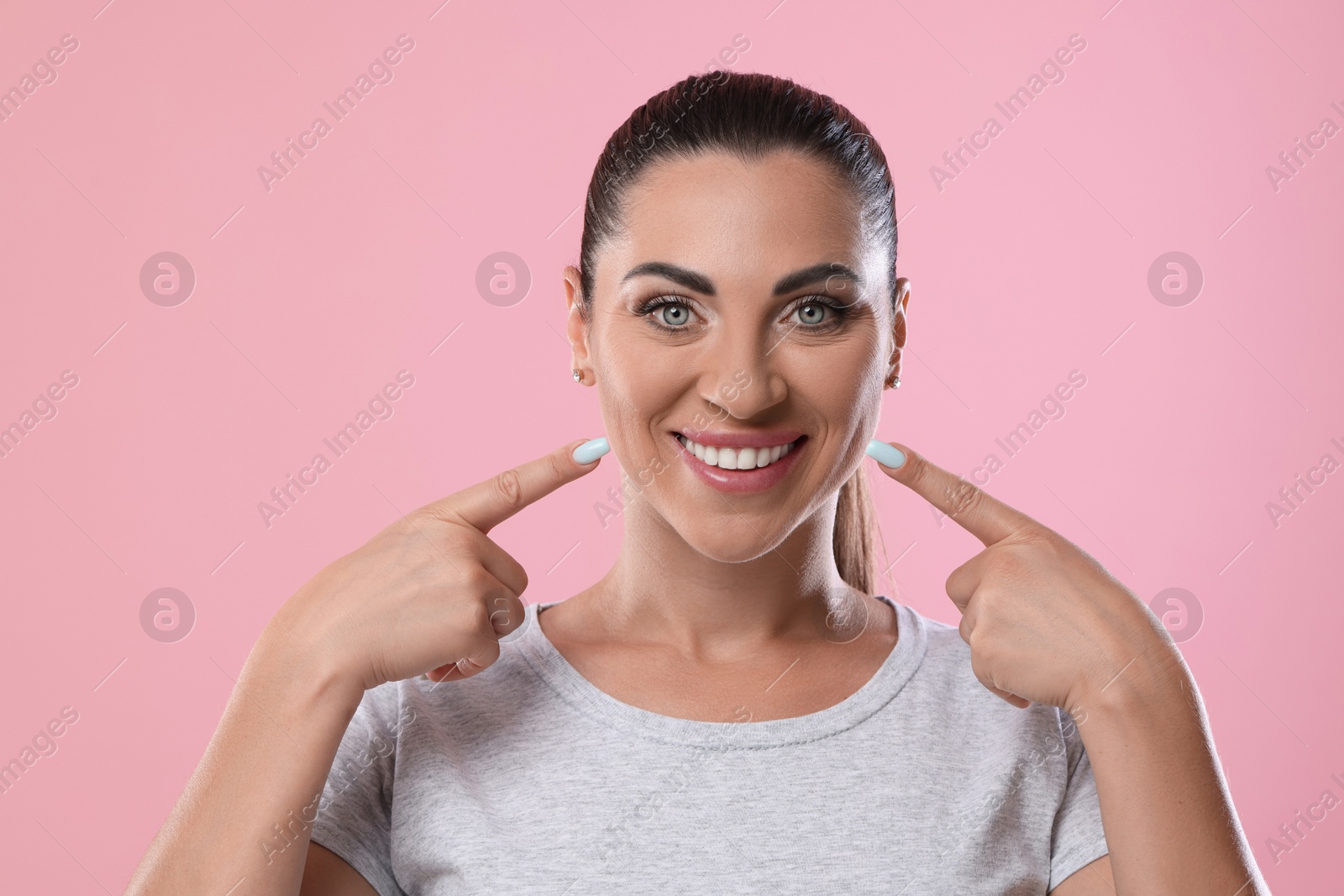 Photo of Woman pointing at her healthy teeth on pink background