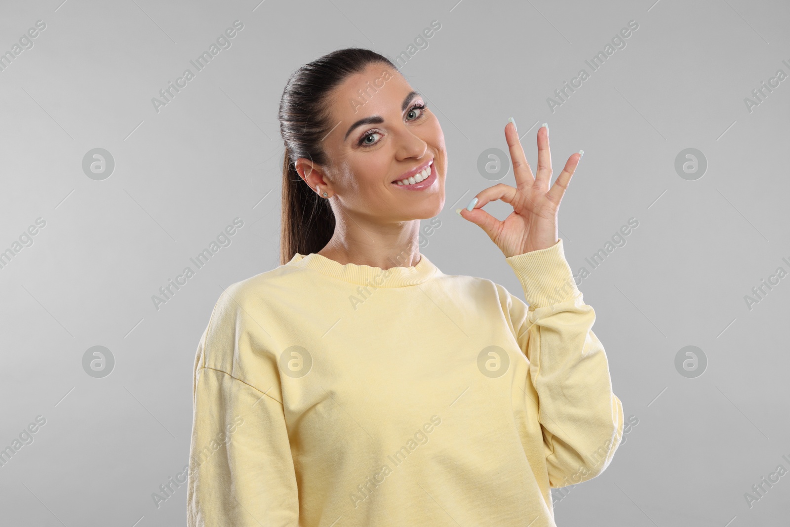 Photo of Woman with perfect healthy teeth showing okay gesture on light grey background