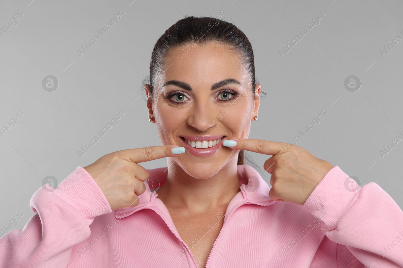 Photo of Woman pointing at her healthy teeth on light grey background