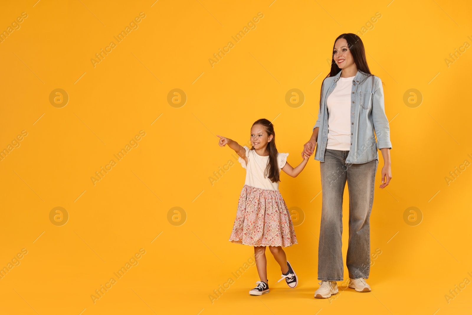 Daughter showing her mother something on yellow background. Space for text Photo of Daughter showing her mother something on yellow background. Space for text