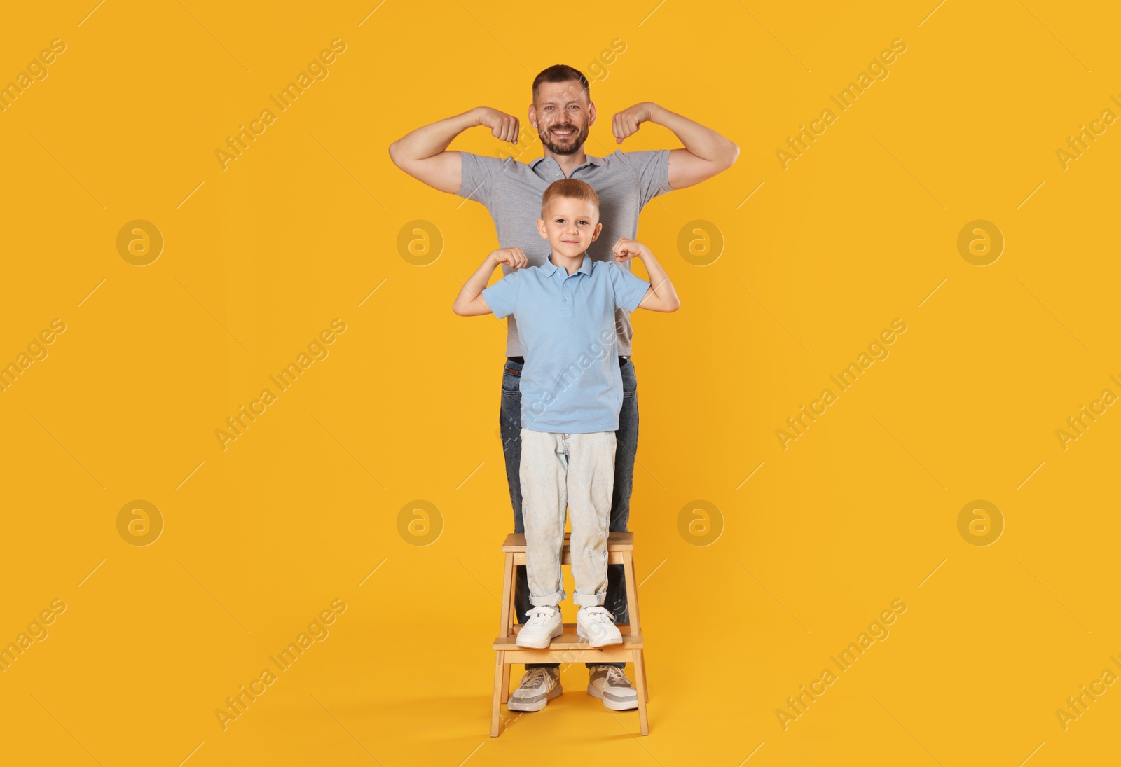Photo of Father and son showing biceps on yellow background