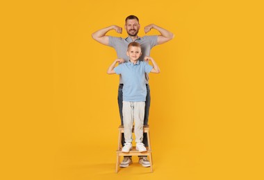 Photo of Father and son showing biceps on yellow background
