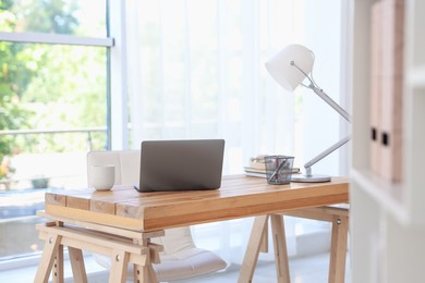 Photo of Home workspace. Laptop and stationery on wooden desk near window indoors