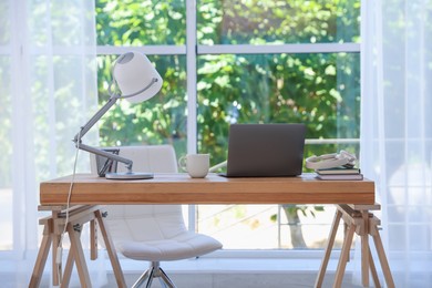 Photo of Home workspace. Laptop and stationery on wooden desk near window indoors