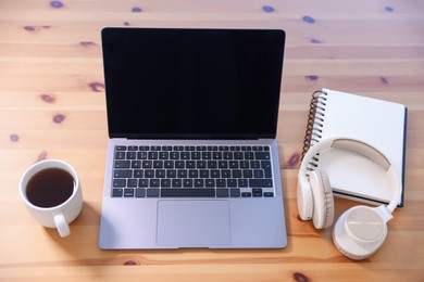 Photo of Home workspace. Laptop, cup of tea, notebook and headphones on wooden desk, above view
