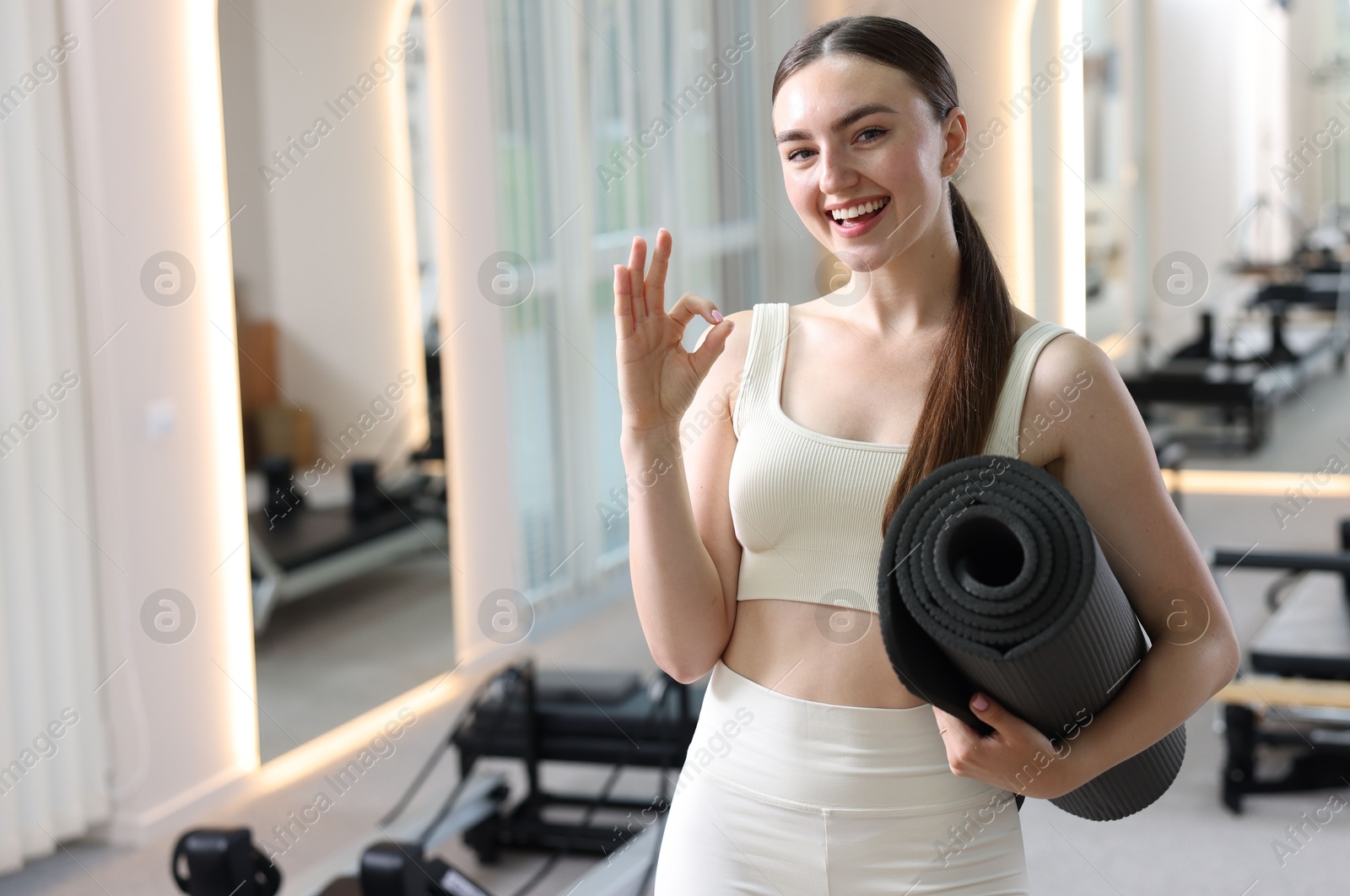 Photo of Woman with fitness mat showing ok gesture in pilates studio, space for text