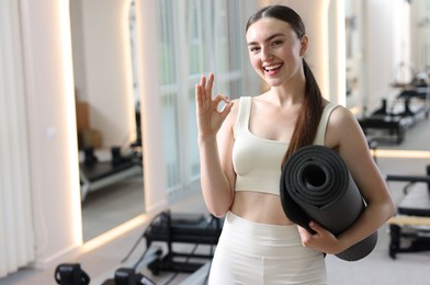 Photo of Woman with fitness mat showing ok gesture in pilates studio, space for text