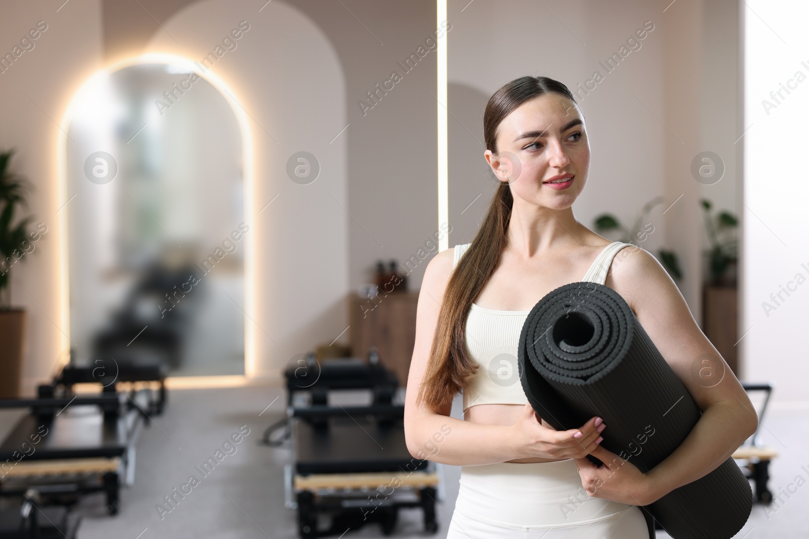 Photo of Woman with fitness mat in pilates studio, space for text