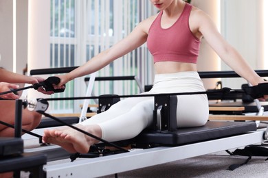 Photo of Woman exercising on reformer supervised by pilates instructor in studio, closeup