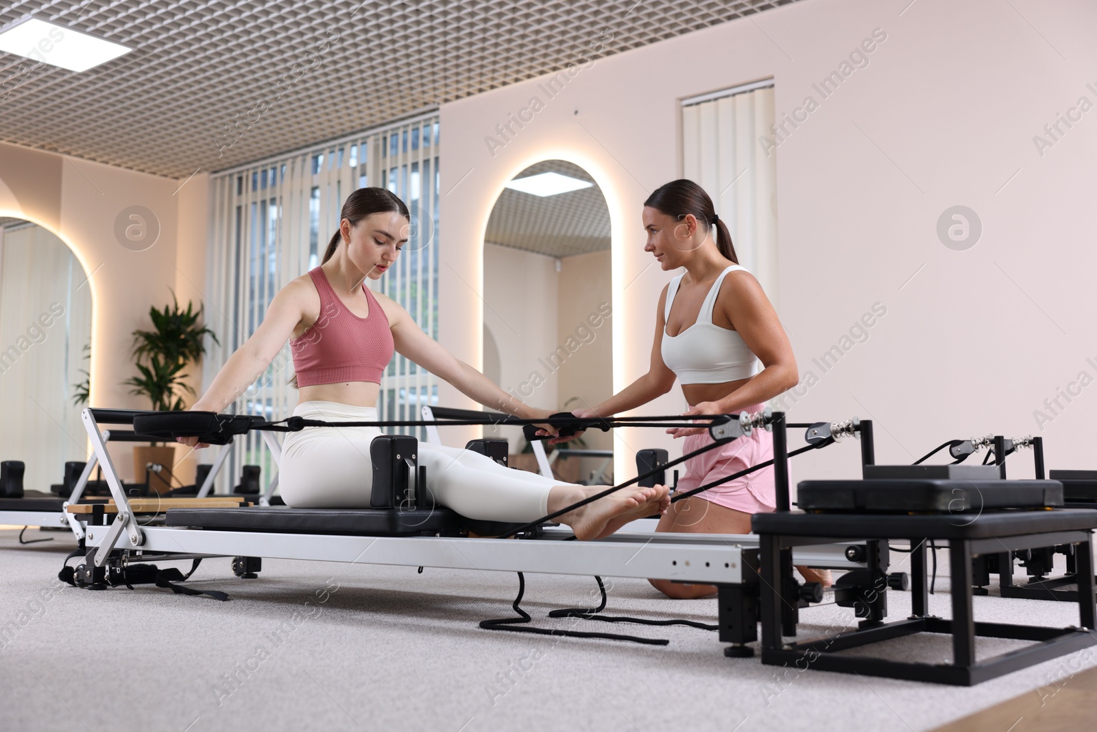 Woman exercising on reformer supervised by pilates instructor in studio Photo of Woman exercising on reformer supervised by pilates instructor in studio