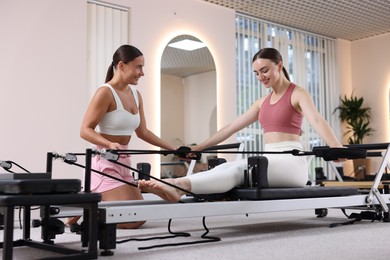 Photo of Woman exercising on reformer supervised by pilates instructor in studio