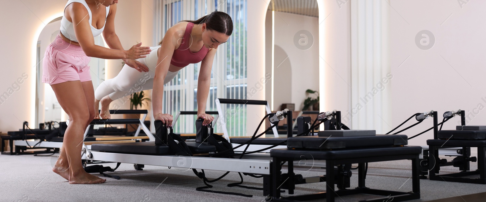 Woman exercising on reformer supervised by pilates instructor in studio Photo of Woman exercising on reformer supervised by pilates instructor in studio