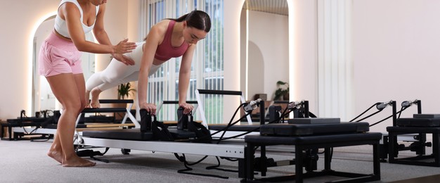 Photo of Woman exercising on reformer supervised by pilates instructor in studio