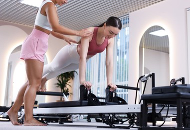 Photo of Woman exercising on reformer supervised by pilates instructor in studio, low angle view
