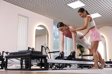 Photo of Woman exercising on reformer supervised by pilates instructor in studio, low angle view