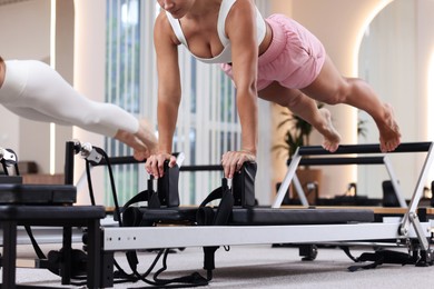 Photo of Woman and pilates instructor exercising on reformers in studio, closeup