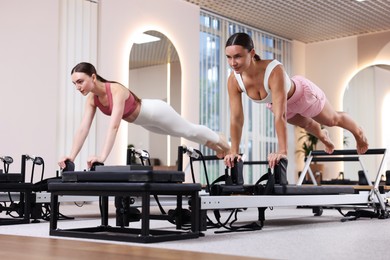 Photo of Woman and pilates instructor exercising on reformers in studio