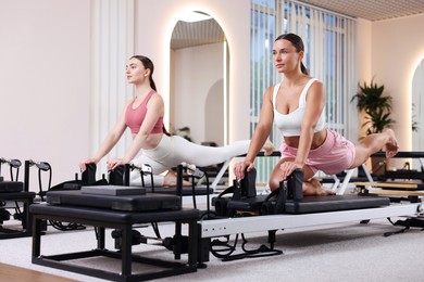 Photo of Woman and pilates instructor exercising on reformers in studio