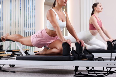 Photo of Woman and pilates instructor exercising on reformers in studio