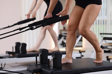 Photo of Woman and pilates instructor exercising on reformers in studio, closeup