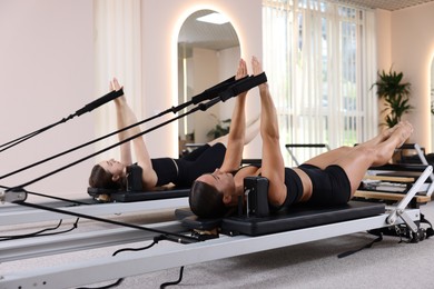Photo of Woman and pilates instructor exercising on reformers in studio