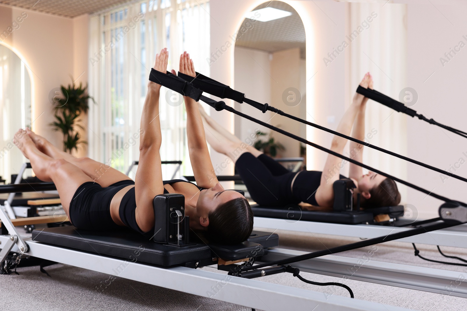 Photo of Woman and pilates instructor exercising on reformers in studio