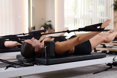 Photo of Woman and pilates instructor exercising on reformers in studio