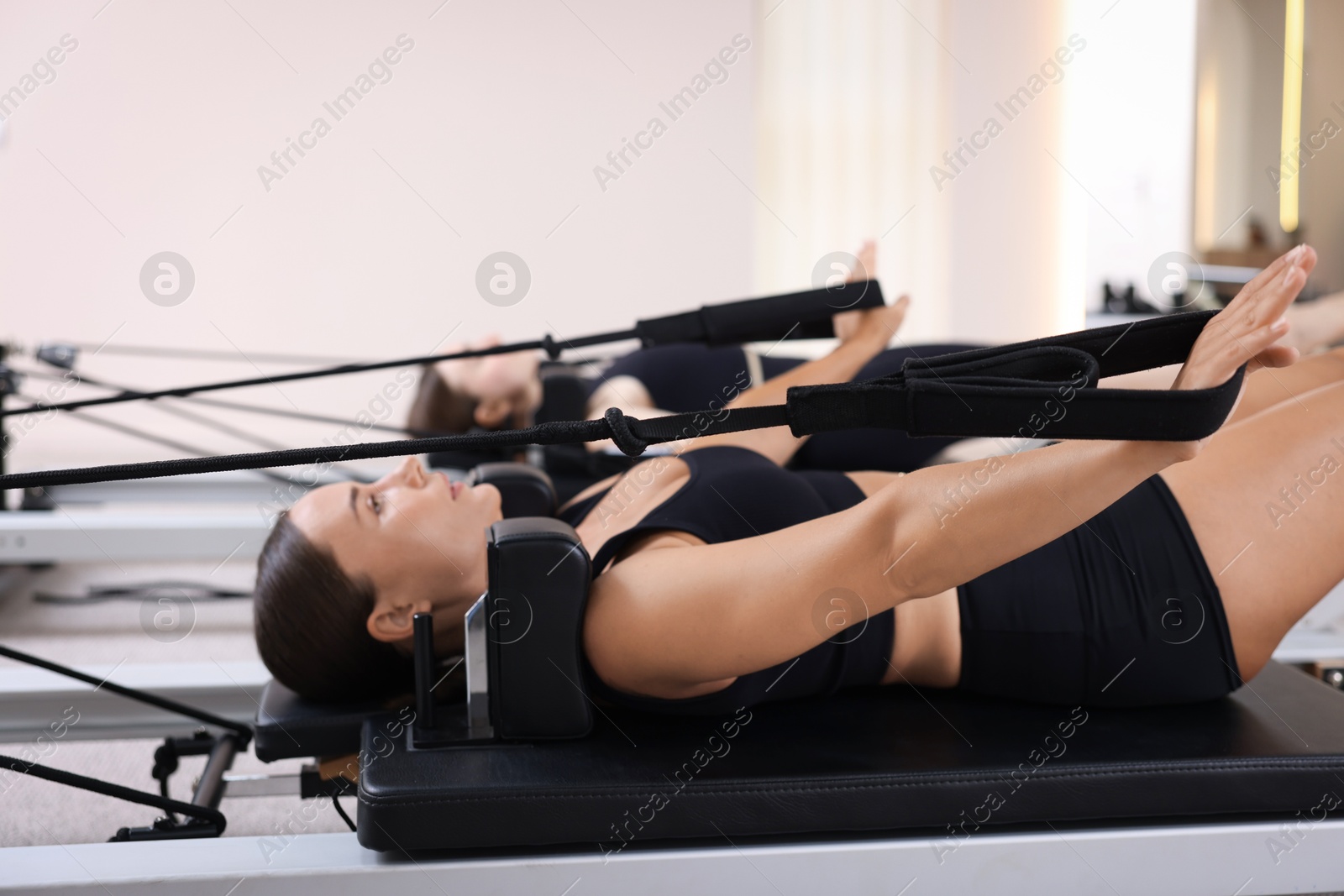 Photo of Woman and pilates instructor exercising on reformers in studio, selective focus