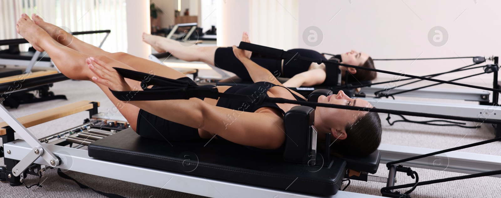 Photo of Woman and pilates instructor exercising on reformers in studio, selective focus