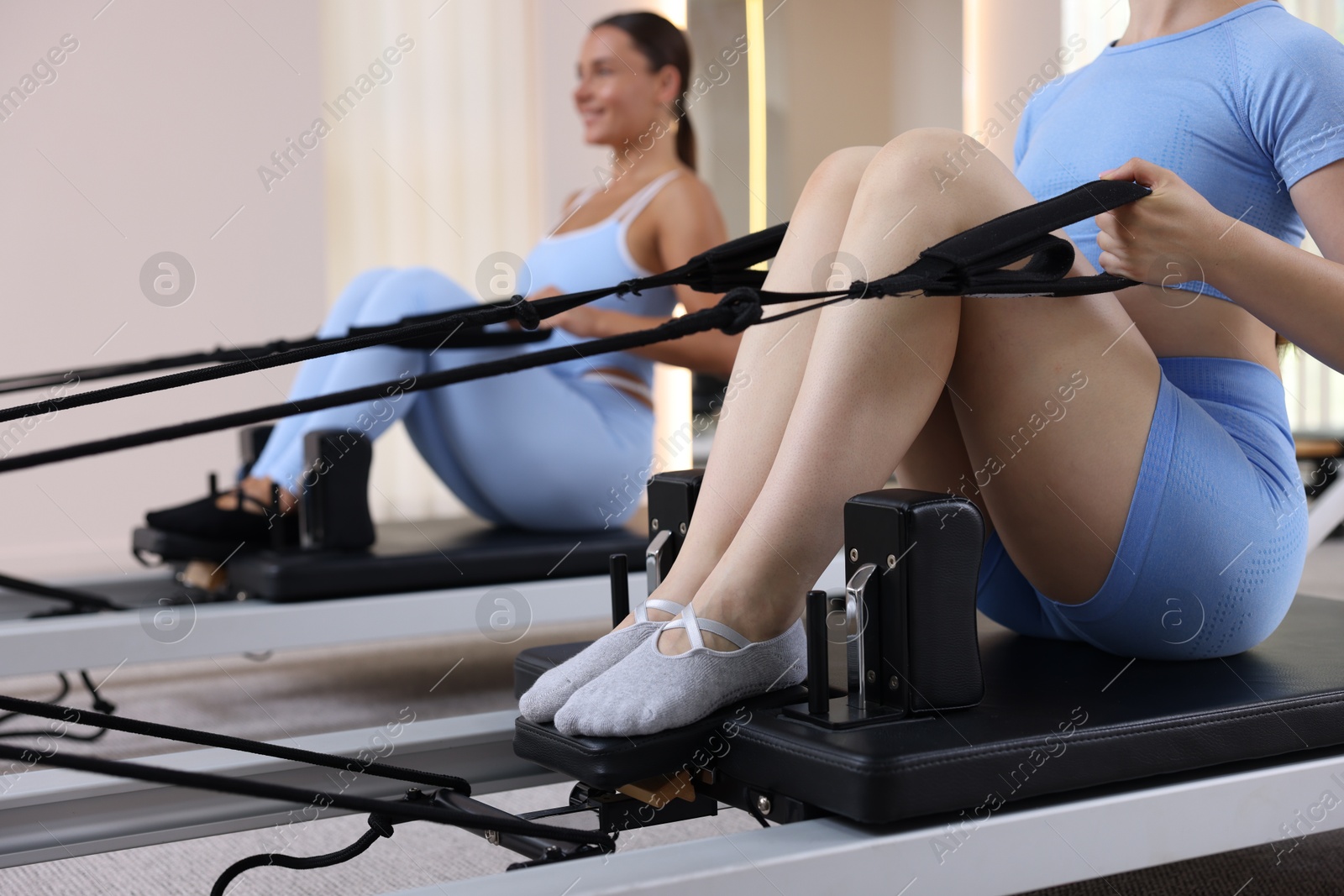 Photo of Woman and pilates instructor exercising on reformers in studio, selective focus