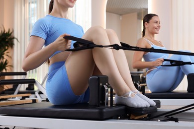 Photo of Woman and pilates instructor exercising on reformers in studio