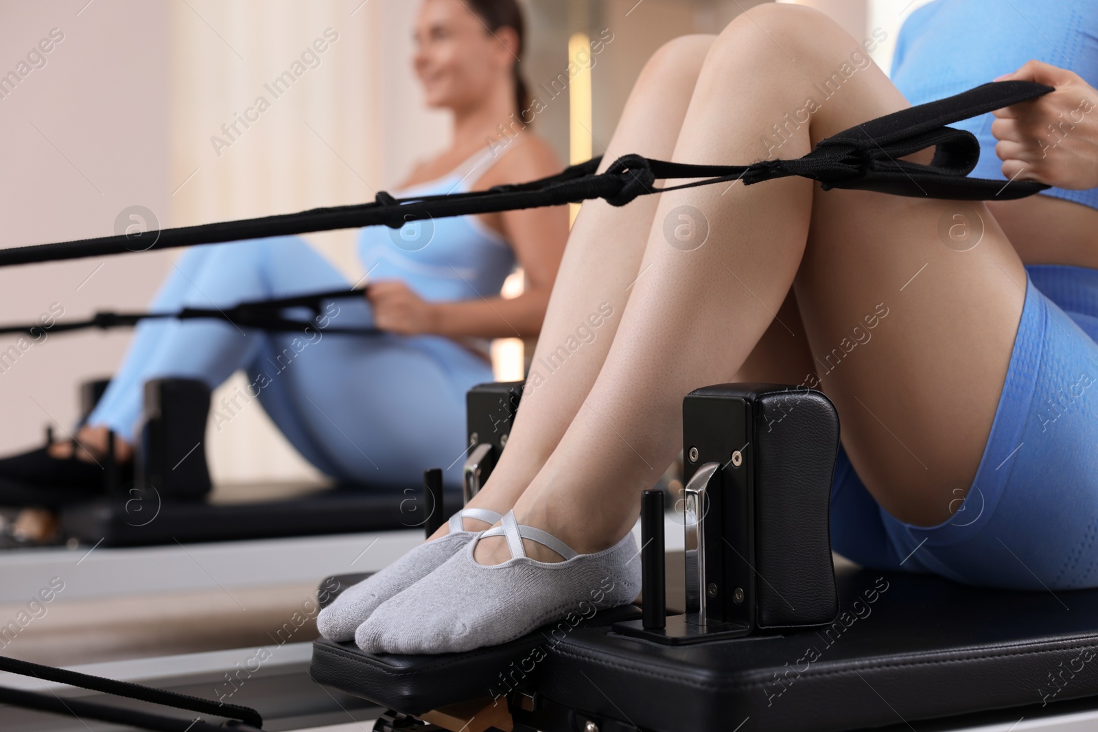 Photo of Woman and pilates instructor exercising on reformers in studio, selective focus