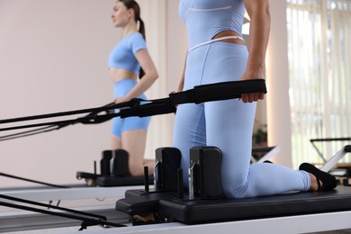 Photo of Woman and pilates instructor exercising on reformers in studio, selective focus
