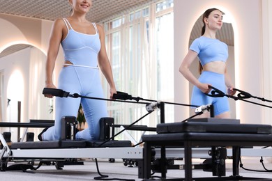 Photo of Woman and pilates instructor exercising on reformers in studio