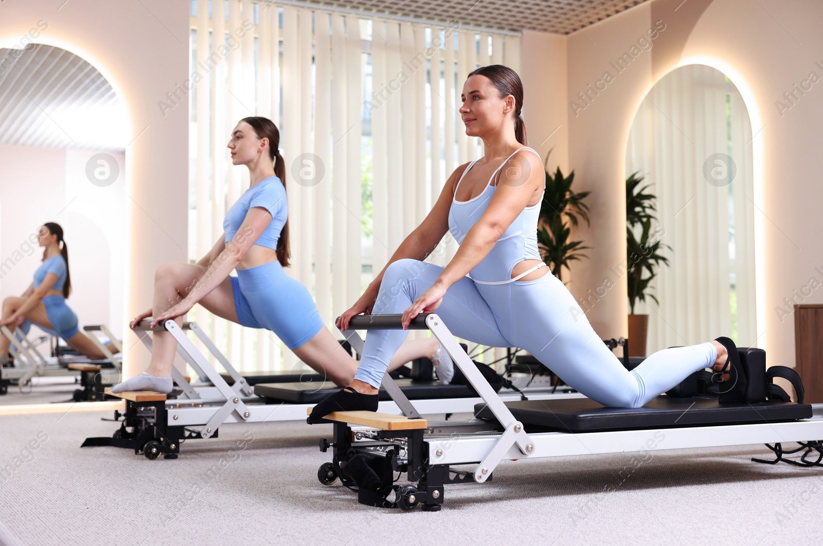 Photo of Woman and pilates instructor exercising on reformers in studio
