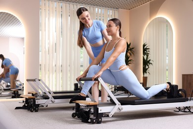 Photo of Woman exercising on reformer supervised by pilates instructor in studio