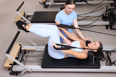 Photo of Woman exercising on reformer supervised by pilates instructor in studio
