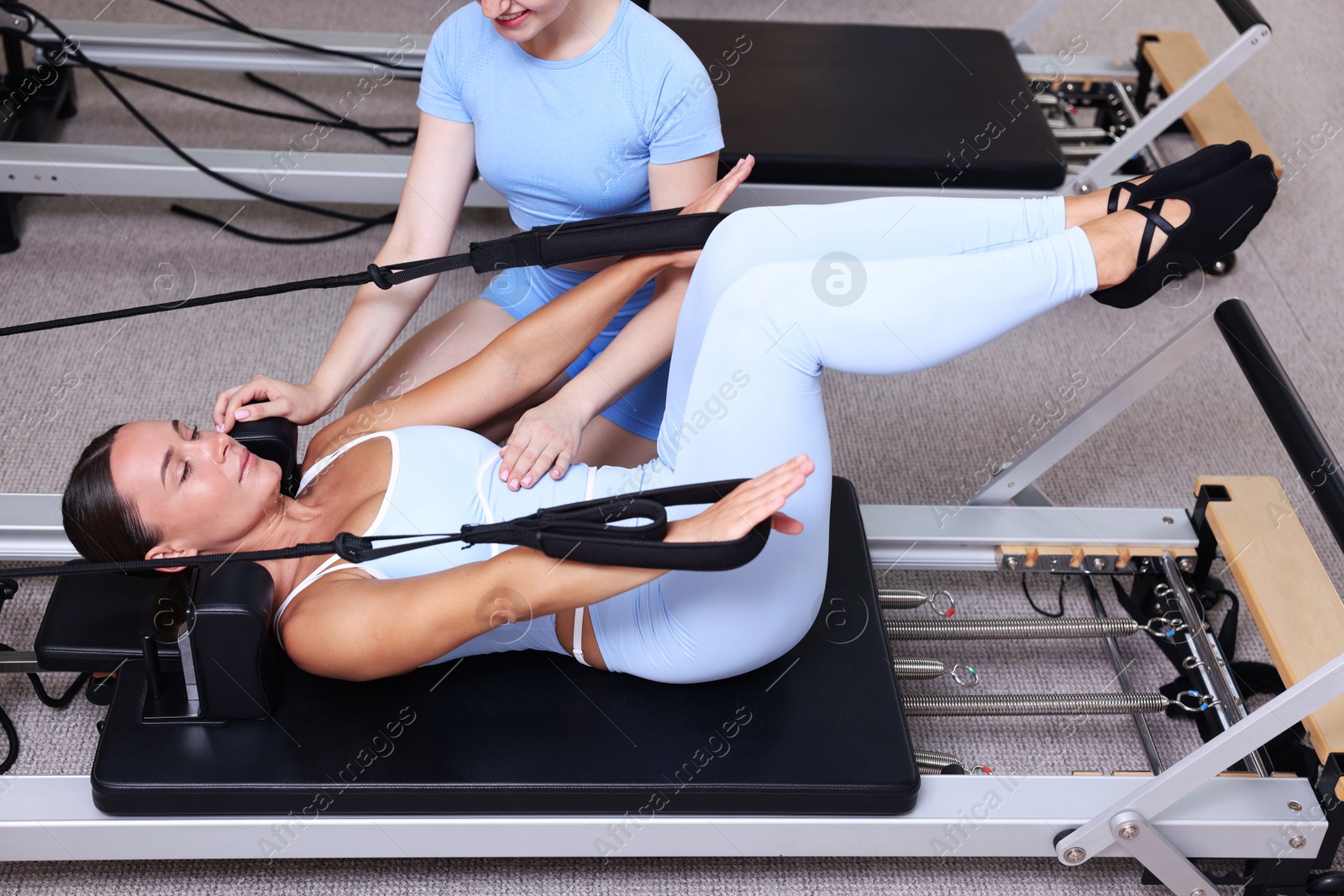 Photo of Woman exercising on reformer supervised by pilates instructor in studio