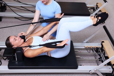 Photo of Woman exercising on reformer supervised by pilates instructor in studio