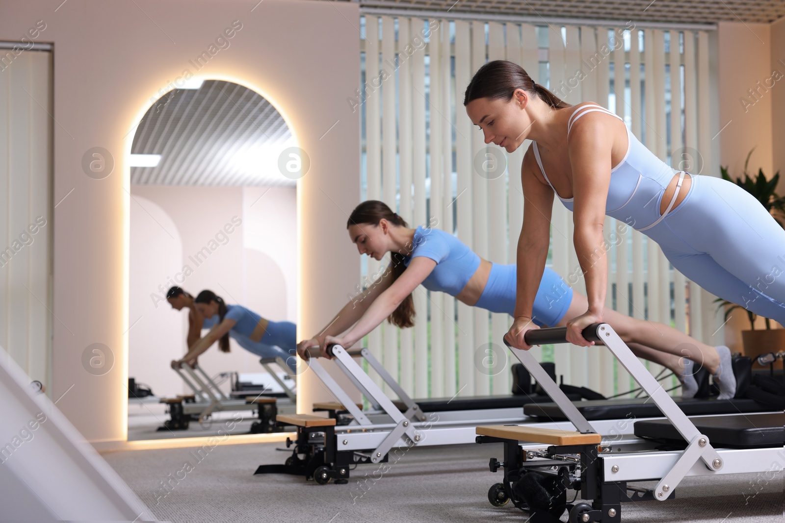 Photo of Woman and pilates instructor exercising on reformers in studio